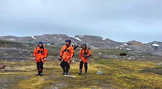 Three scientists in orange jackets walking on Svalbard