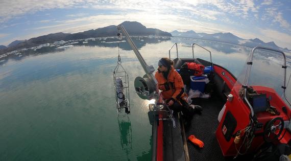 Scientist on boat lowering a device into Arctic water