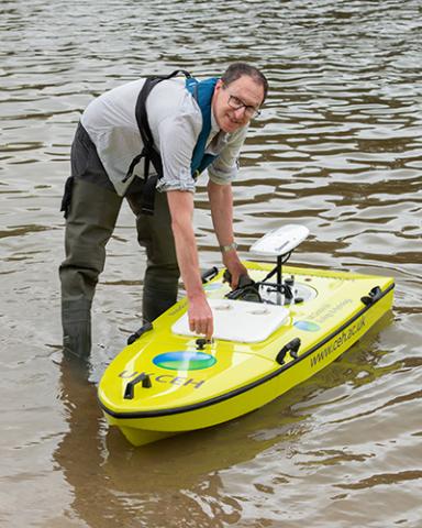 Nick Everard standing in a river with the remote controlled Arcboat 
