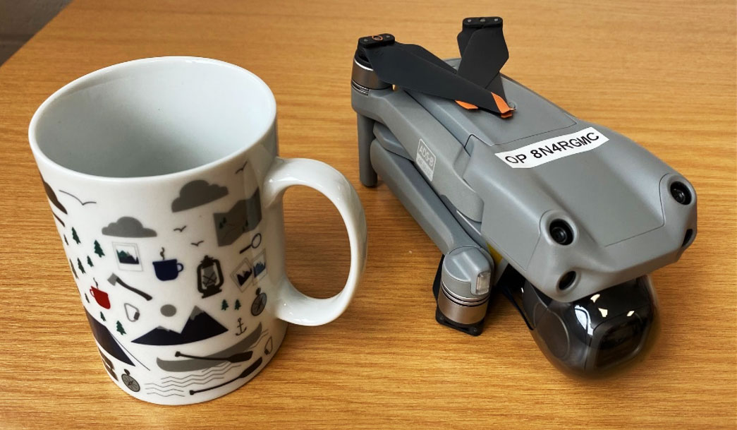 Small drone sitting on a table beside a tea mug to show scale