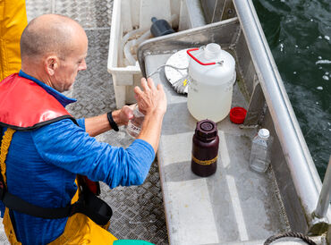 Monitoring of Windermere A man pours a water sample into a flask aboard a metal boat