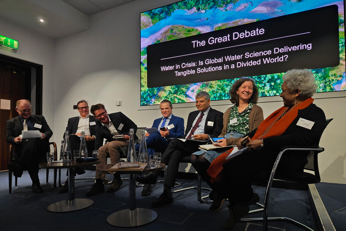 Seven people seated on a stage in front of a large presentation screen