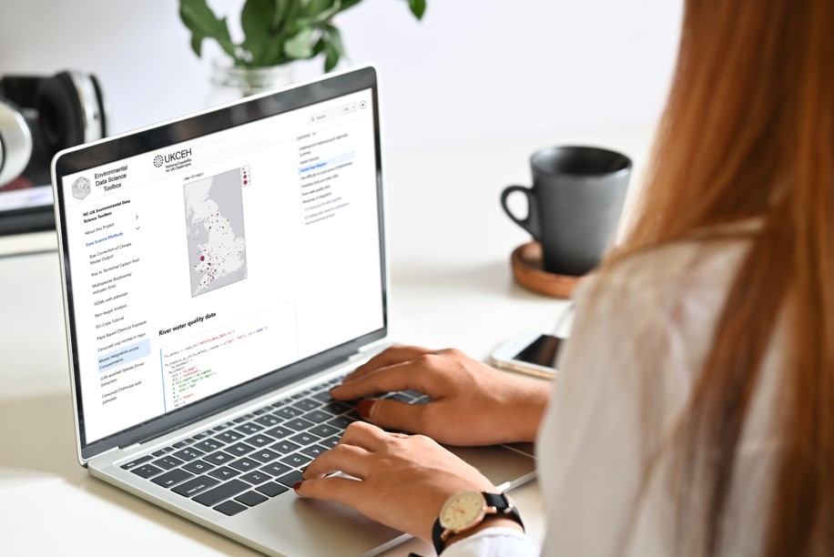 Environmental Data Science Toolbox Woman with long hair sitting typing on a laptop with the toolbox on the screen with a map and writing