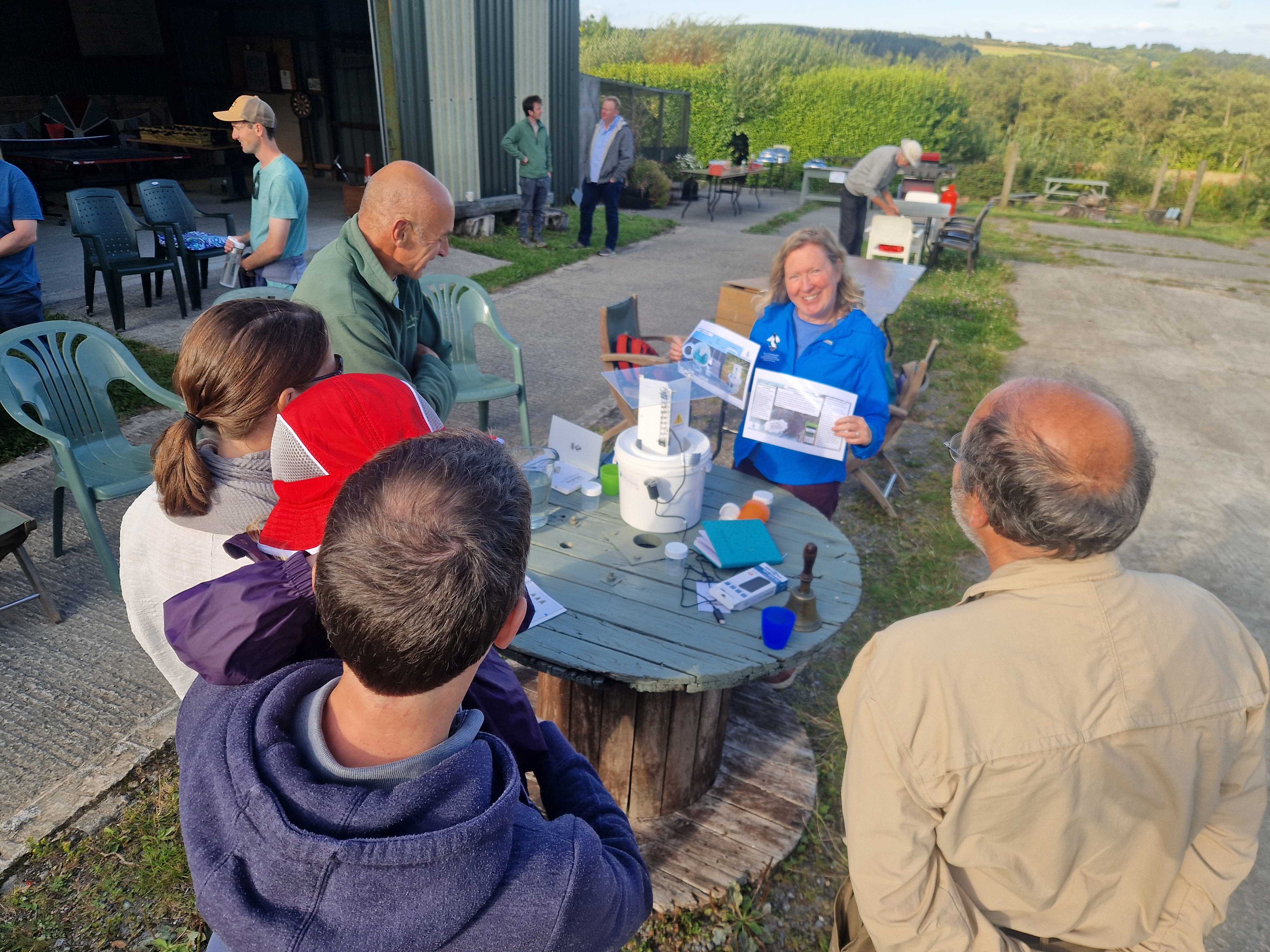 Image of 4 people surrounding a table with a LED bucket trap on it, with a facilitator showing the instructions of how to use the equipment and the app