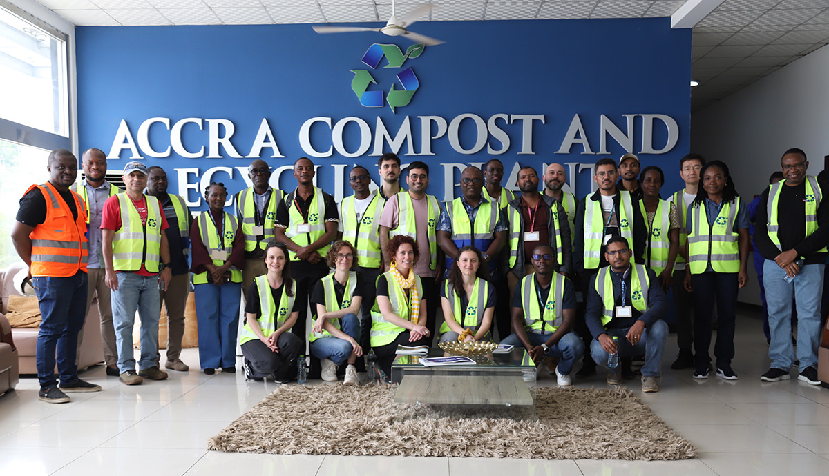 Large group of people wearing hi-viz jackets gathered in front of a sign saying Accra Compost and Recycling Plant