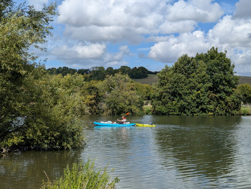 Person rowing a kayak upstream with a remote controlled boat alongside