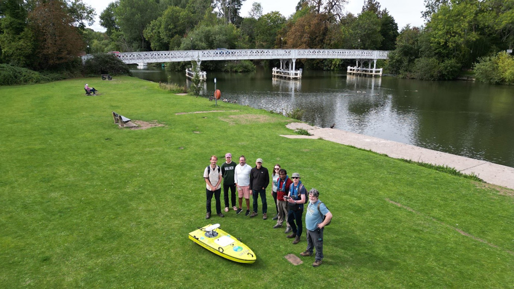 Drone view of a group of 8 people including the drone operator standing near a river