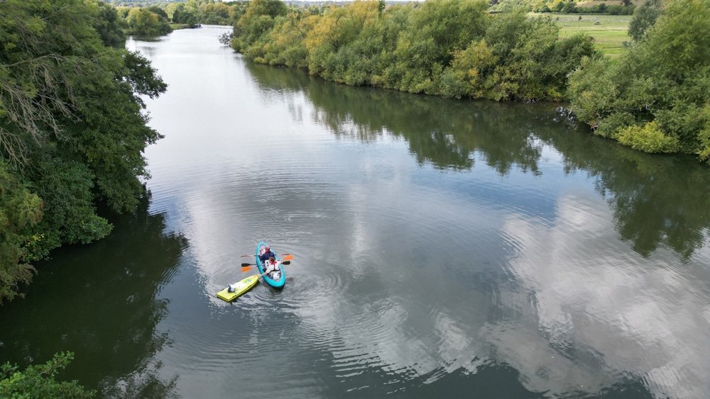Aerial view of a kayak with two people on board beside a remote controlled boat on a river