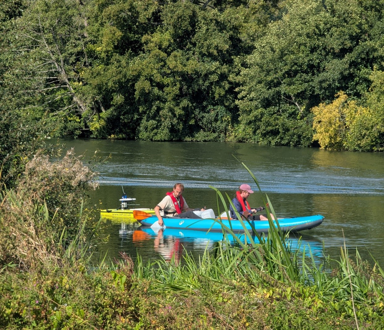 Two people in a kayak on a river, one sampling water