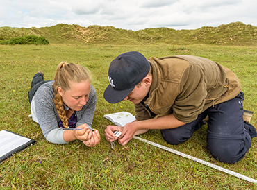 Undertaking fieldwork for sand dunes research. Photo by Daniel Hauck Two people surveying a patch of grassland