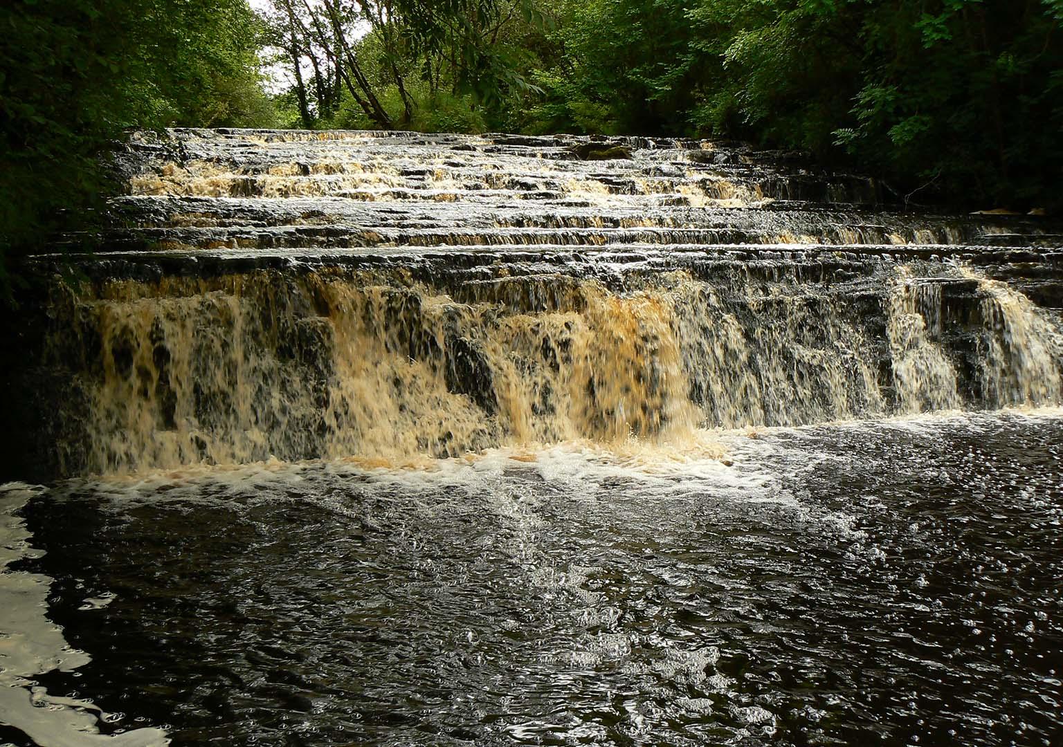 Brown coloured water flowing over a weir