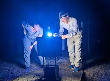Two researchers examining an automated biodiversity monitoring station at night