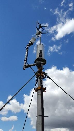 Looking upwards at a tripod flux tower with a clouded blue sky behind