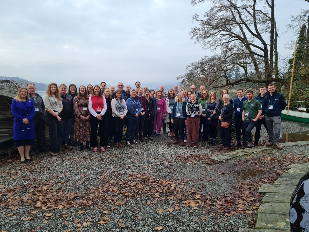 Large group of people standing outside with a glimpse of Windermere in the background