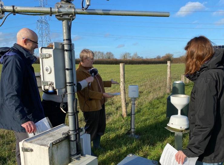 Three people look at scientific equipment placed in a field