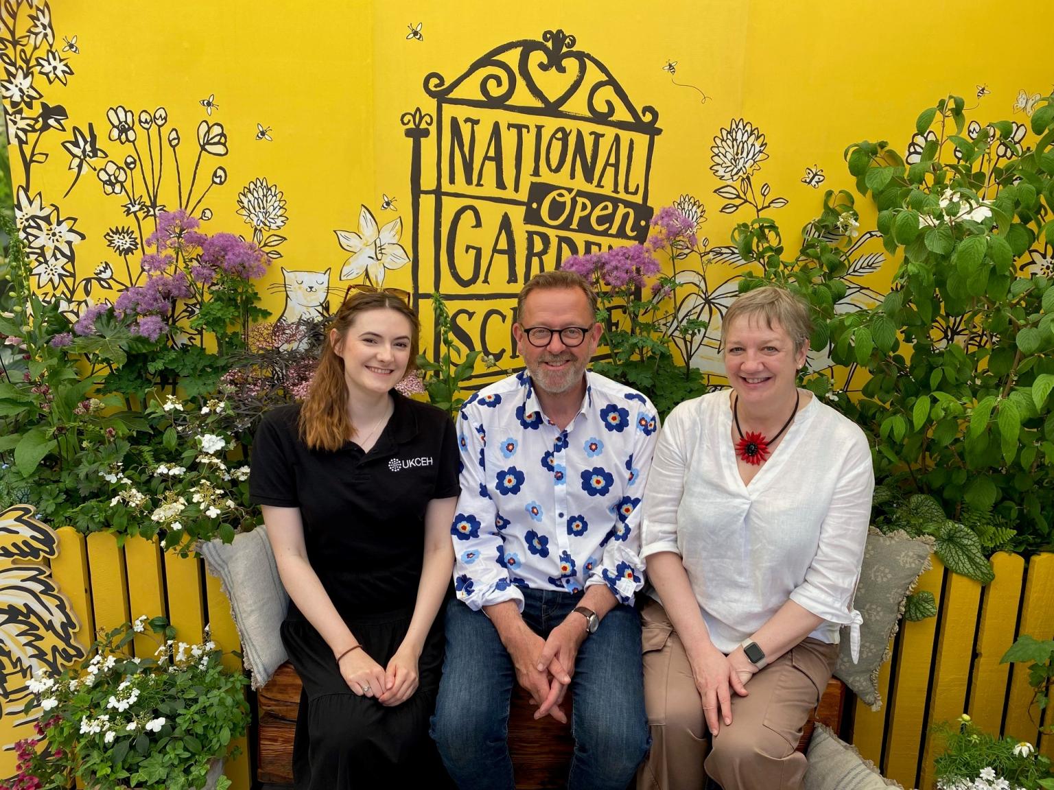 3 people sitting on a bench with plants in background