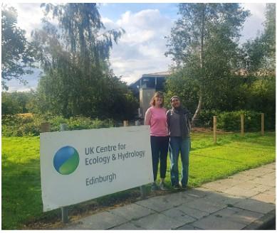 Two women standing alongside a UKCEH sign with grass and a building behind