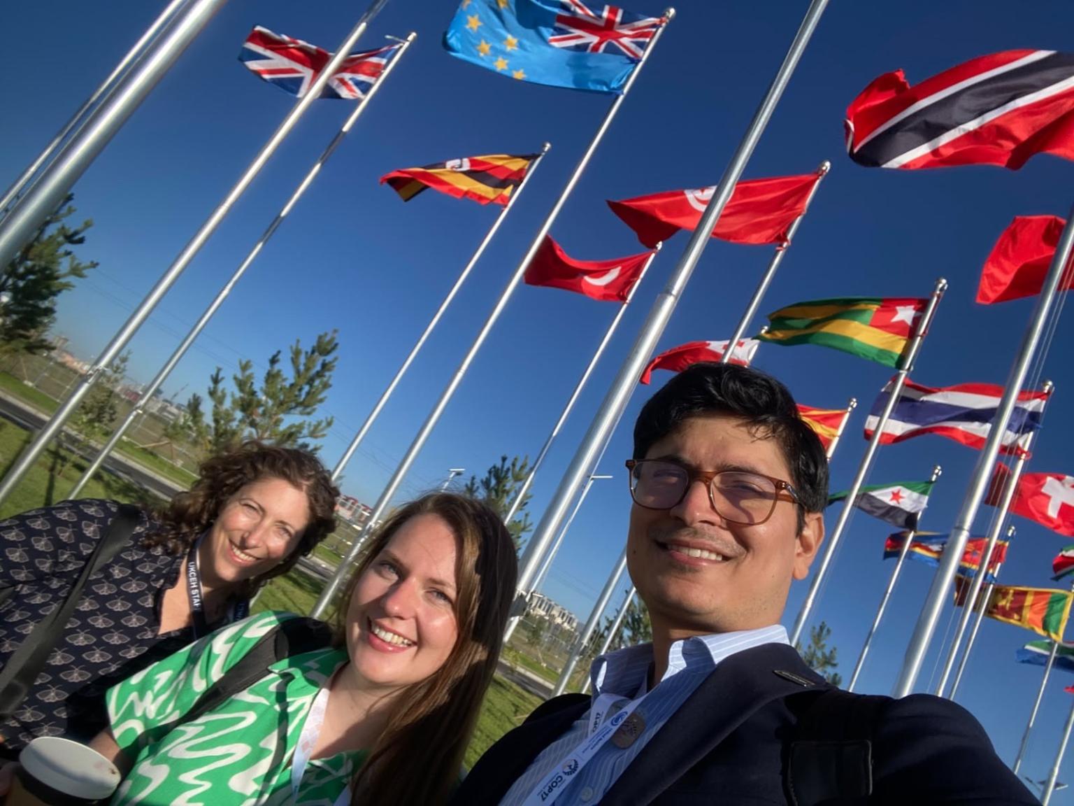 Three people stood in front of a flag