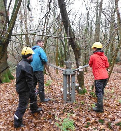 Three people using a coring device in a woodland to extract soil