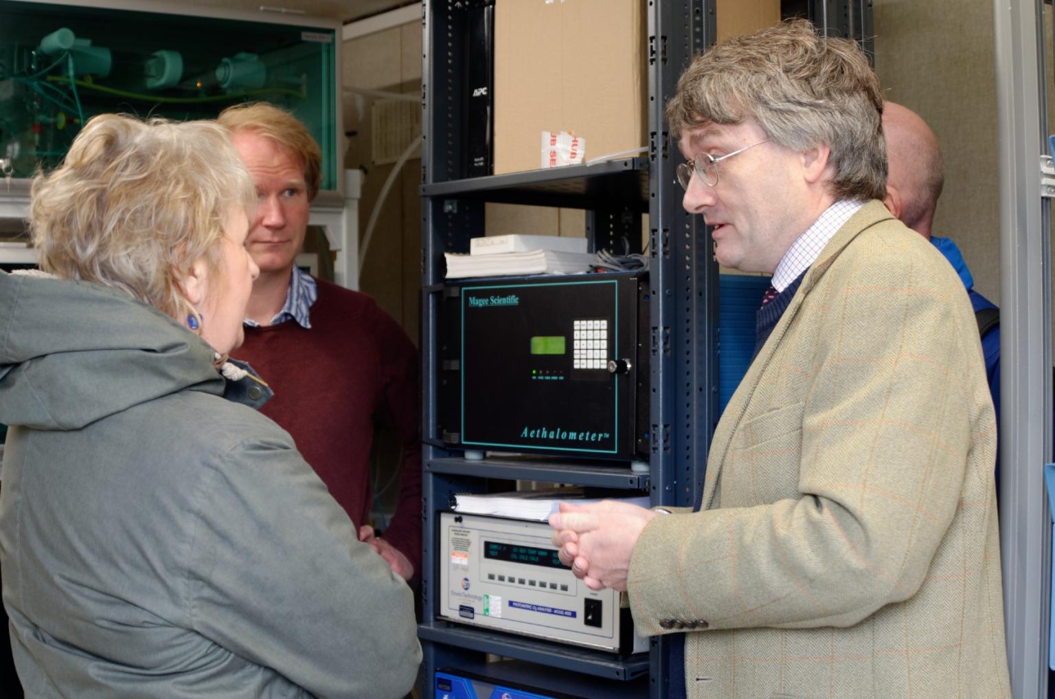 People standing beside scientific equipment in conversation