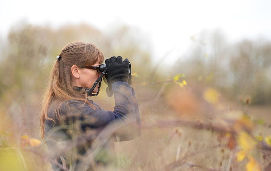 Woman in a field looking through binoculars (photo by Ben Andrew, rspb-images.com