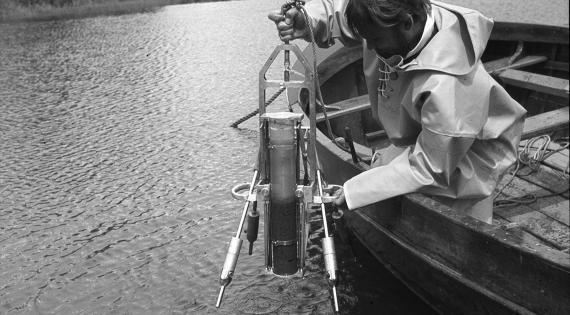 Black and white image of a person in a boat sampling water from Loch Leven