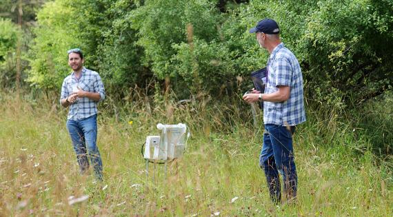 Two UKCEH scientists in a farm field beside a biodiversity monitoring station