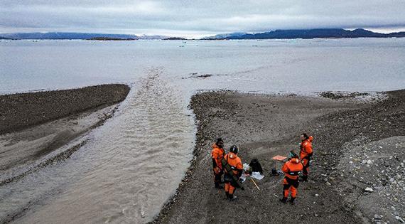 Looking down on four scientists standing beside glacier river