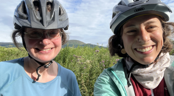 Katrin Kaltenegger and Ulli Dragosits smile wearing bicycle helmets in front of a field