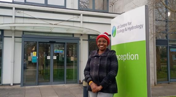 Jemimah Gacheru at UKCEH Jemimah Gacheru stands in front of the UKCEH sign wearing a grey coat and woolly hat
