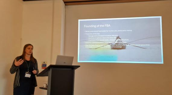 Person stands beside lectern with presentation slide in the background