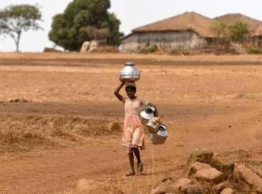 Girl carrying water container on her head in a drought landscape in Maharashtra State, India