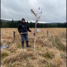 Person standing next to a weather station in a field