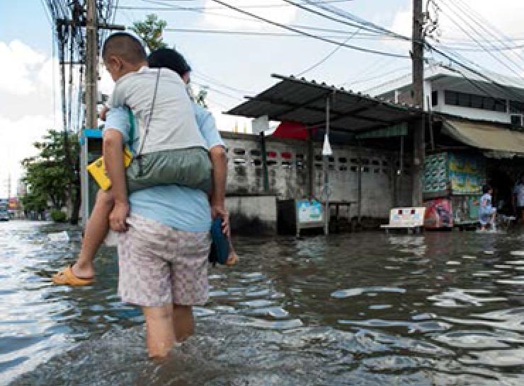 Child being carried on the back of a person walking through flood waters