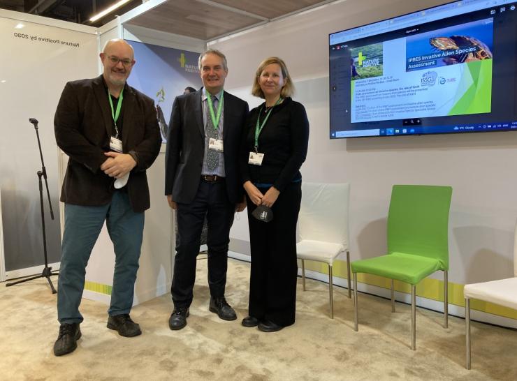 Three people standing beside a large monitor screen