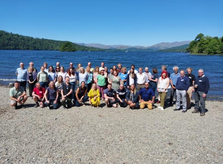 Group of more than 40 people standing by Windermere under blue skies