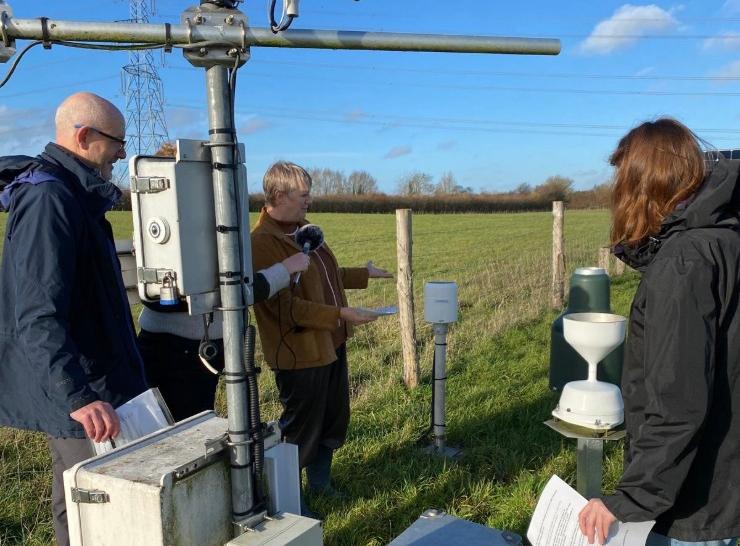 Three people look at scientific equipment placed in a field