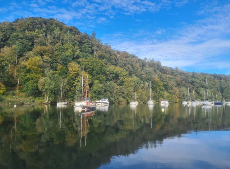Lake in the foreground with a hill covered in trees and some boats on the lake